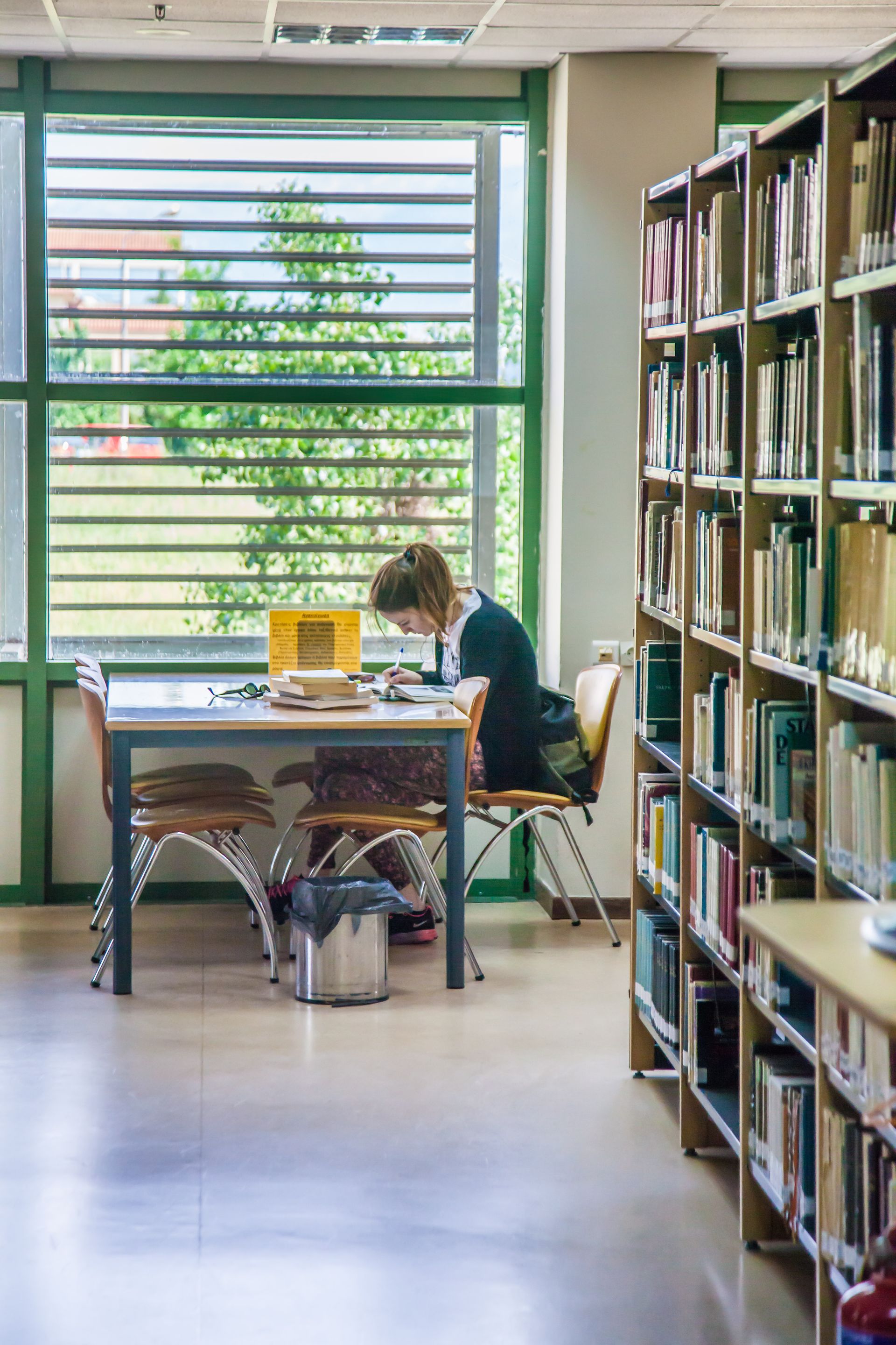 Persona leyendo en una mesa de biblioteca, junto a estantes con libros